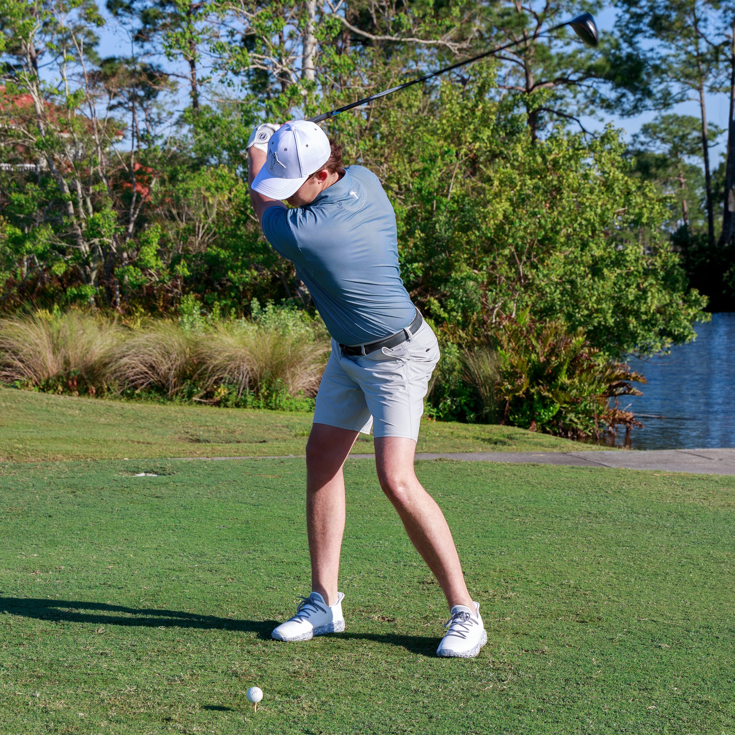 man attempting a golf swing in anderson ord performance apparel, wearing a striped navy golf polo, and anderson ord AO Wave 1 Performance Shoes