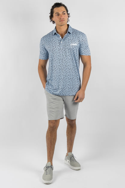 A man modeling a light blue short-sleeve polo shirt with a white abstract pattern, paired with light gray shorts and gray sneakers, against a light gray studio background.