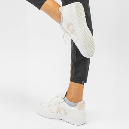 White low-top sneakers with beige AO logo, shown on a model wearing black pants against a clean white studio background.