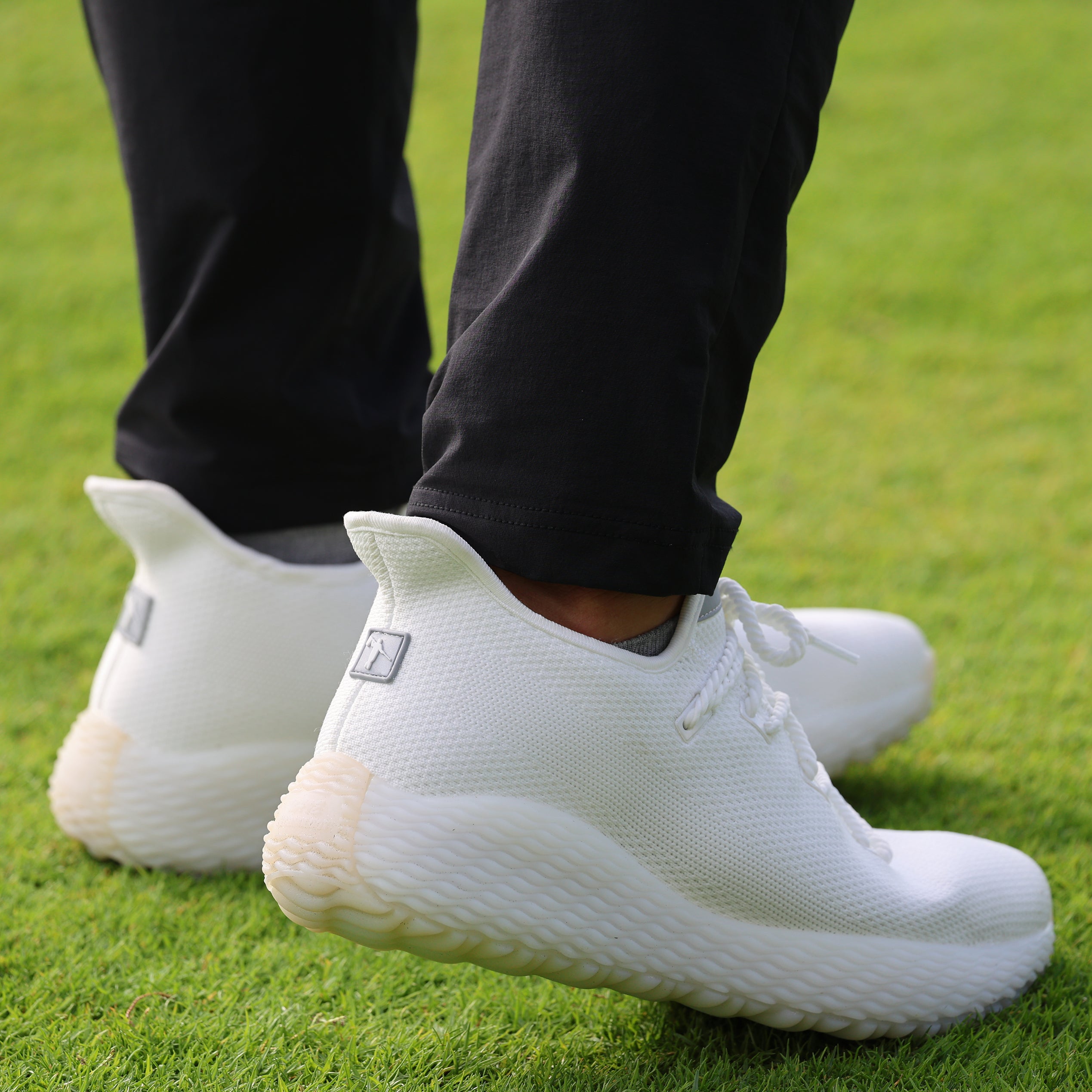 Man on fairway wearing black leggings and white golf shoes. Best mens casual golf shoe. Lifestyle running shoe. The AO WAVE1, the Ultimate Crossover Performance Shoe.